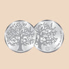 Two silver coins with tree and bird designs on a dark purple background