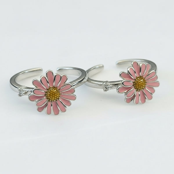 Two silver rings with pink daisy flower designs on a white background