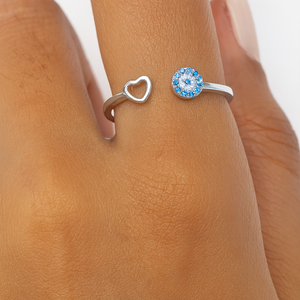 Silver ring with a heart design and another ring with a blue gemstone on a person's finger.