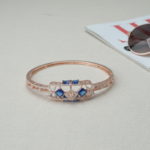 Rose gold bracelet with blue stones on a light surface with sunglasses and magazine in the background