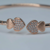 Rose gold bangle with heart-shaped ends on a light blue background