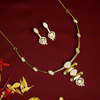 Gold necklace and earrings on a red background with decorative leaves.