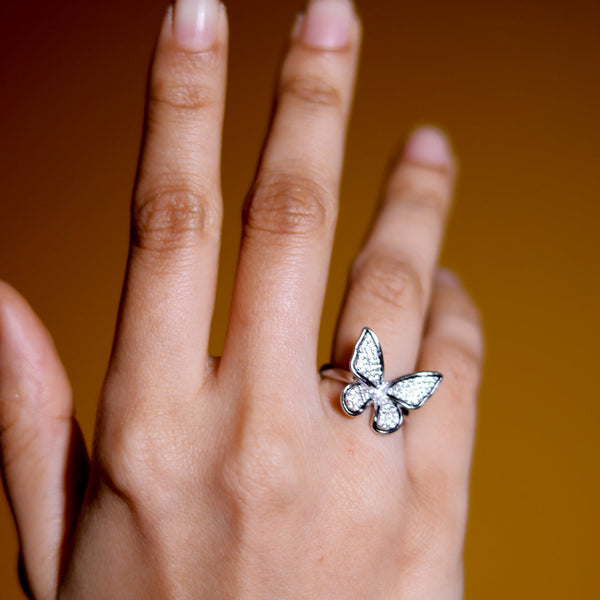 Hand wearing a butterfly ring against a warm brown background