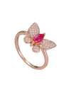 Rose gold butterfly ring with a red gemstone on a marble surface