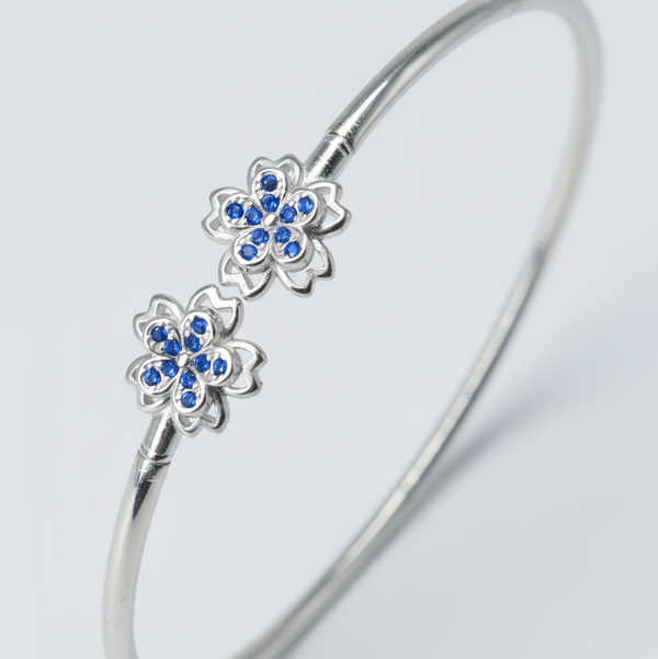 Silver bangle with blue gemstone flowers on a gray background