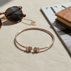 Rose gold bracelet with sunglasses and a book on a textured surface