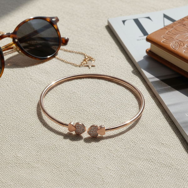 Rose gold bracelet with sunglasses and a book on a textured surface